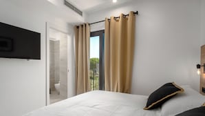 A bedroom with a bed, a TV mounted on the wall, and a window with curtains.