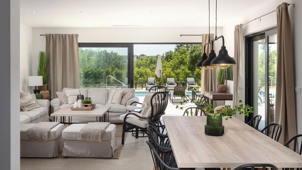 A spacious living room with a large window, a dining area, and a pool view.