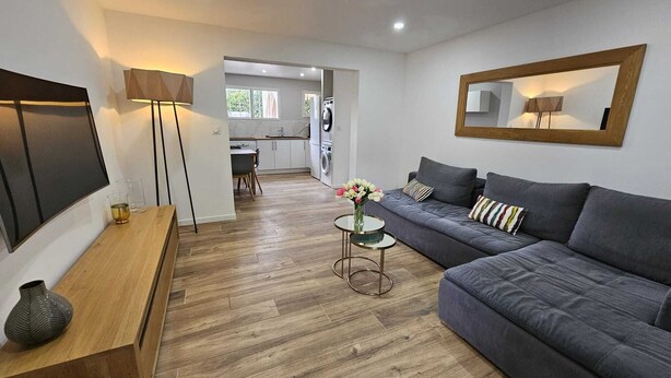 A modern living room with a grey sofa, a wooden coffee table, a TV, and a kitchen in the background. - 3-bedroom house for 4 people (Aix-en-Provence)
