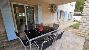 An outdoor patio with a glass table and metal chairs, a potted plant, and a sliding glass door leading to a kitchen. - 3-bedroom house for 4 people (Aix-en-Provence)