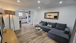 A modern living room with a grey sofa, a coffee table, and a floor lamp. There is a kitchen area in the background with a washing machine and a sink. - 3-bedroom house for 4 people (Aix-en-Provence)