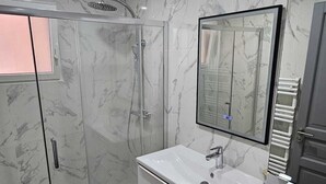 A modern bathroom with a glass-enclosed shower, a white vanity with a mirror, and marble-patterned walls. - 3-bedroom house for 4 people (Aix-en-Provence)