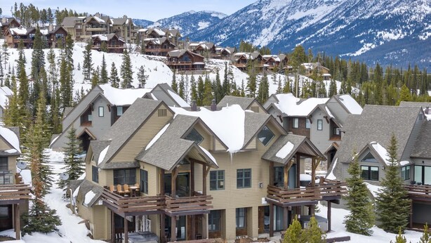 A resort with multiple chalet-style buildings, wooden balconies, and a snowy mountainous backdrop. - Ski-In/Ski-Out via Pony Express Lift (Big Sky)