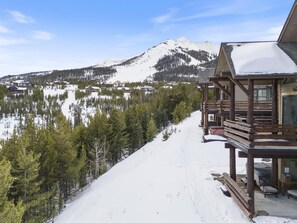 A wooden cabin with a balcony overlooking a snowy mountain and a lake.