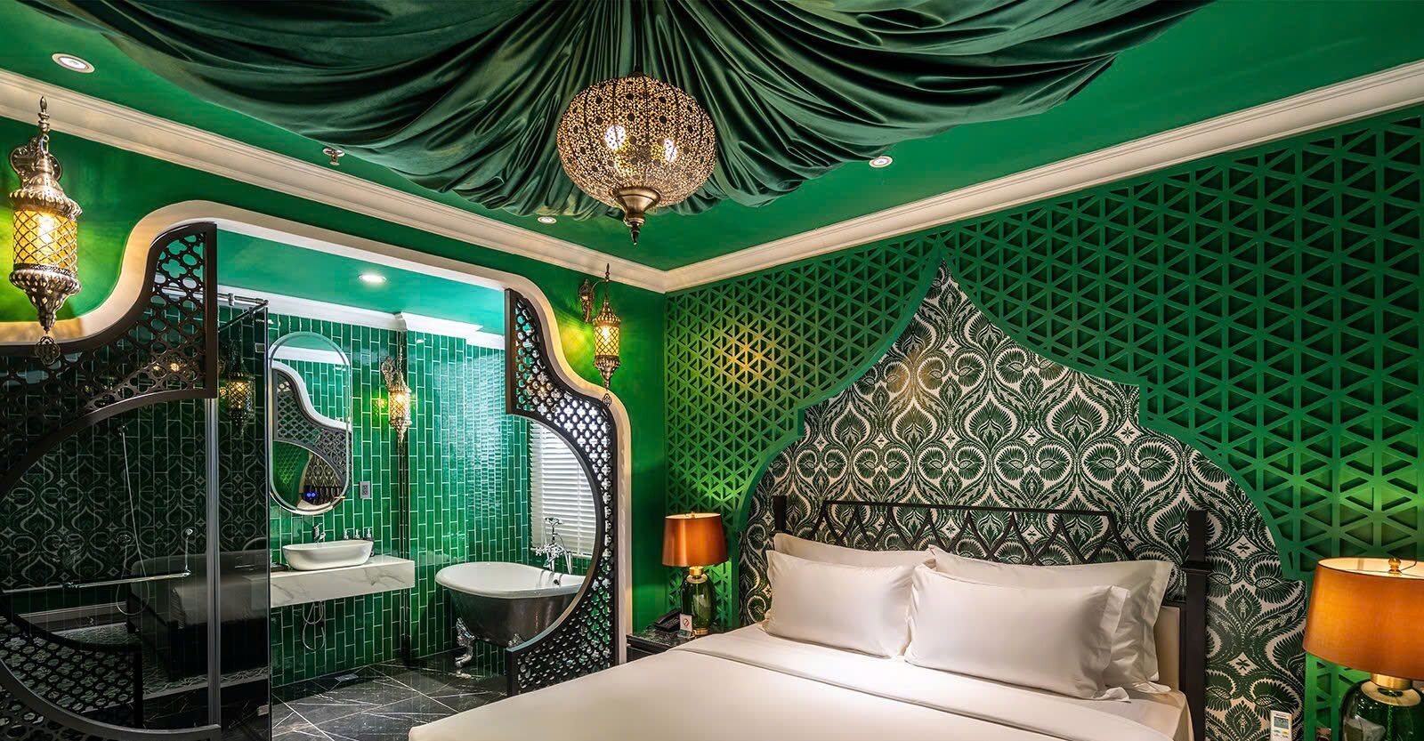 A luxurious room with a green color scheme, a large ornate bed, a round mirror, and a modern bathroom with a sink and bathtub.