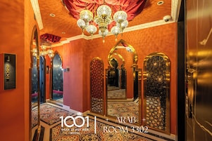 Um corredor luxuoso com espelhos ornamentados, um candelabro e piso coberto por carpete.