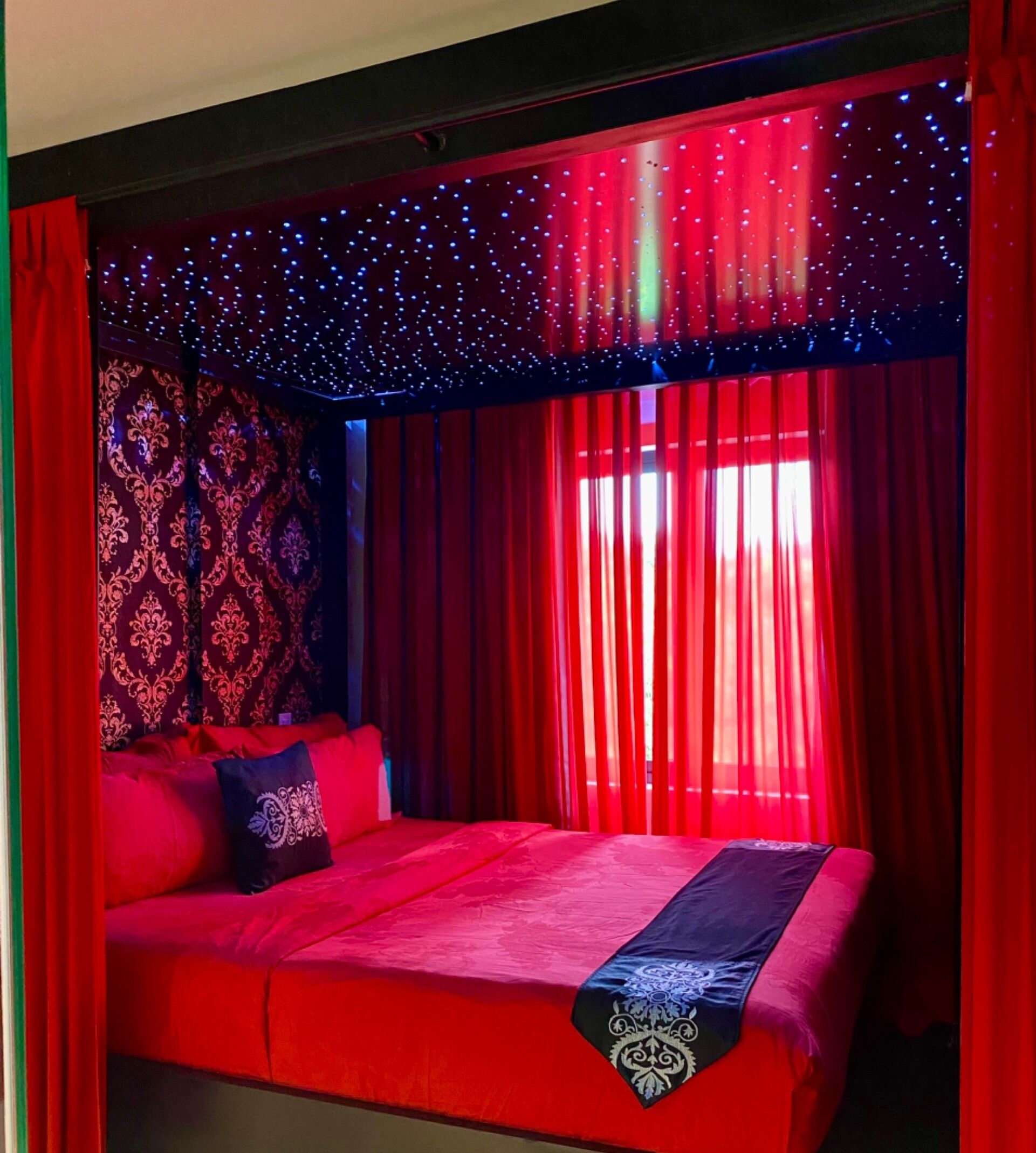 A room with a bed, red curtains, and a patterned wall.