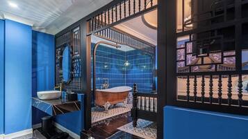 Une salle de bain aux murs bleus, avec un lavabo blanc, une baignoire sur pieds d’époque et un carrelage noir et blanc.