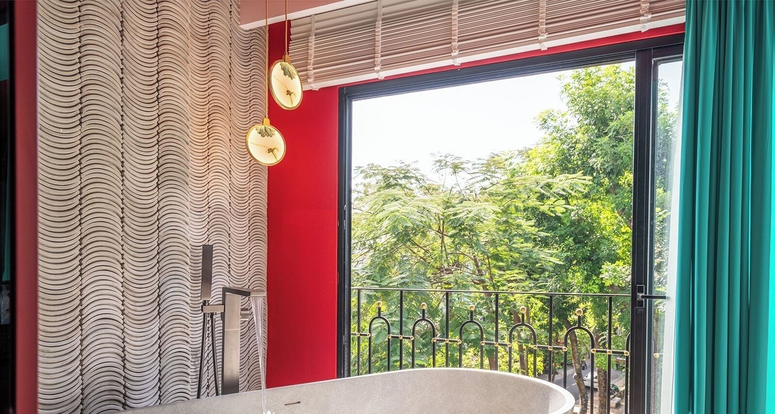 Une salle de bain avec une baignoire sur pieds, un mur d’accent rouge et une vue sur la verdure grâce à une grande fenêtre.