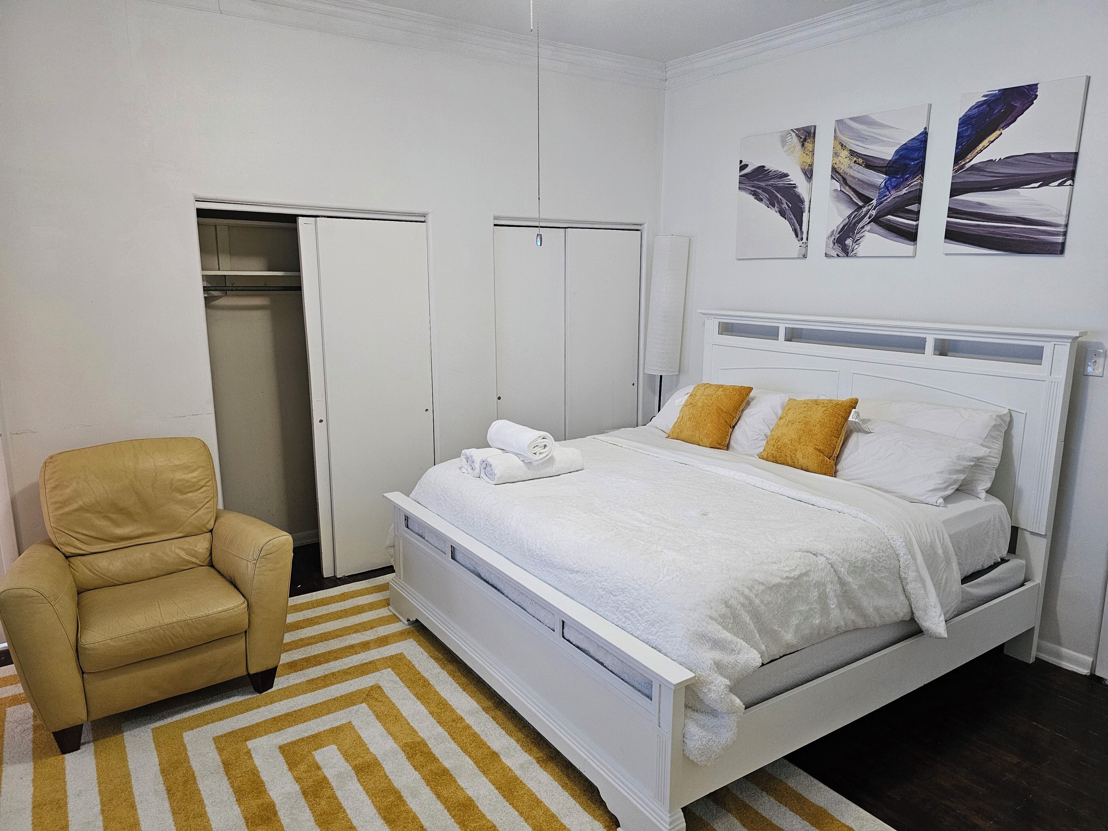 Una camera da letto con un letto, una sedia, un armadio e opere d'arte alle pareti.