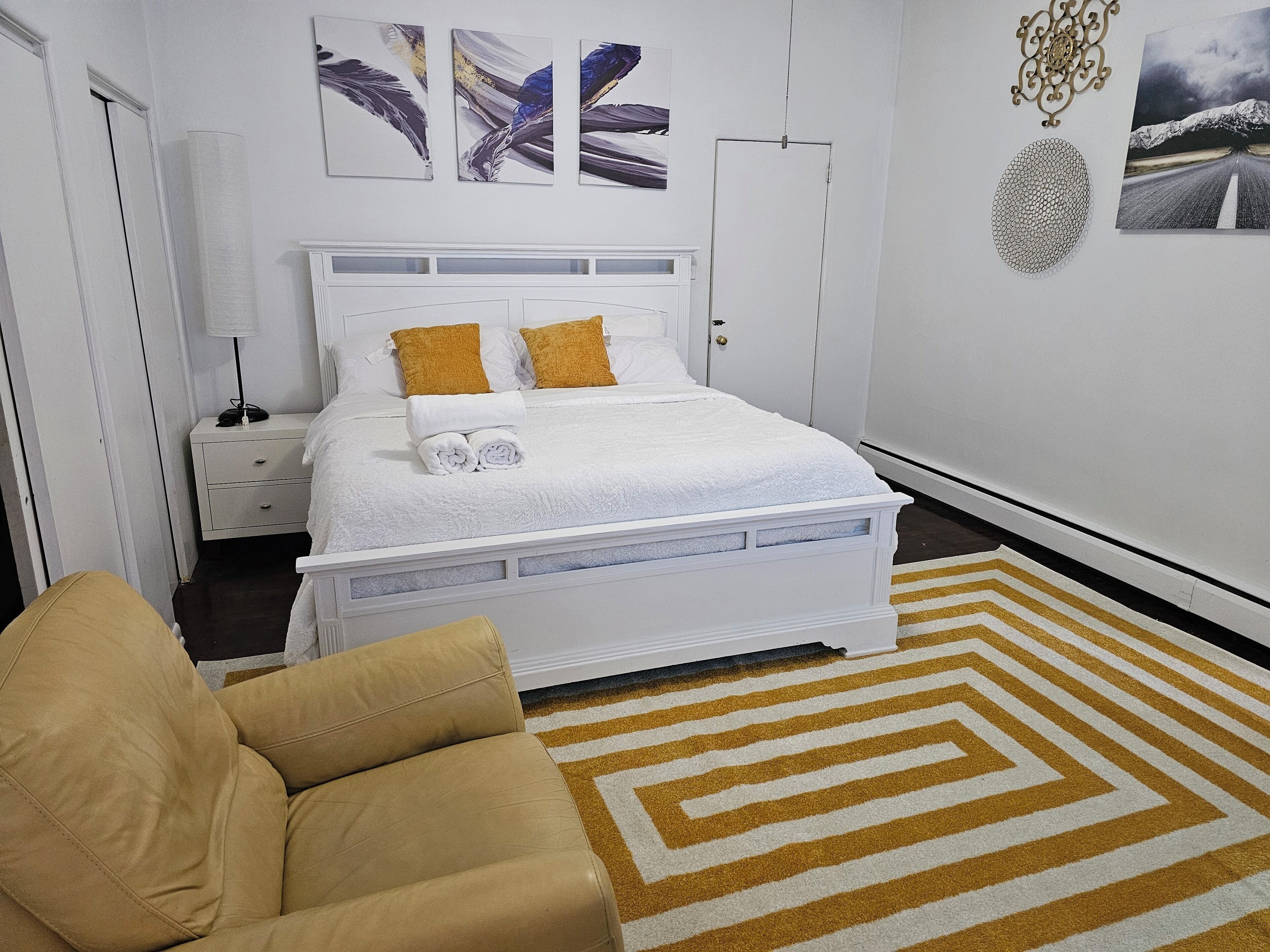 Un dormitorio ordenado con cama, mesita de noche, lámpara y silla.