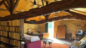 Een rustieke kamer met houten plafond, een bed, een sofa, een tafeltje en een boekenplank vol boeken.