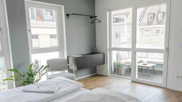 A modern bedroom with two beds, a desk, and a large sliding glass door leading to a balcony. - Perfect city center location, 107 sqm, directly at the opera house in suite flair with balcony! (Nürnberg)