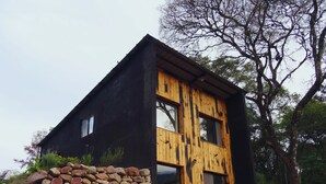 A modern house with a black exterior and wooden accents, surrounded by greenery and a stone wall. - Modern House in Nature at Villa Monte Reserve (Palma Sola)