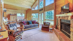 Interior acogedor de una cabaña de madera con chimenea, ventanas amplias y una zona de estar confortable.