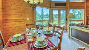 Comedor de cabaña de madera con una mesa dispuesta para cuatro, ventanas amplias y una araña.
