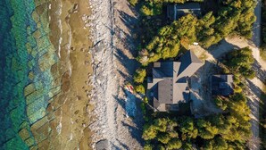 Vista aérea de una propiedad costera con una casa, un litoral rocoso y árboles densos.