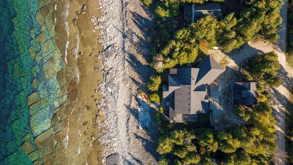 Vue aérienne d’une propriété située sur la côte, avec une maison, un rivage rocheux et une végétation dense.