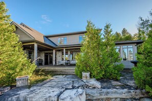 Une maison moderne avec une façade en pierre, un patio couvert doté d’un espace salon extérieur et un jardin bien entretenu.