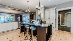 Una cocina moderna con una isla central, taburetes de bar, electrodomésticos de acero inoxidable e iluminación colgante.