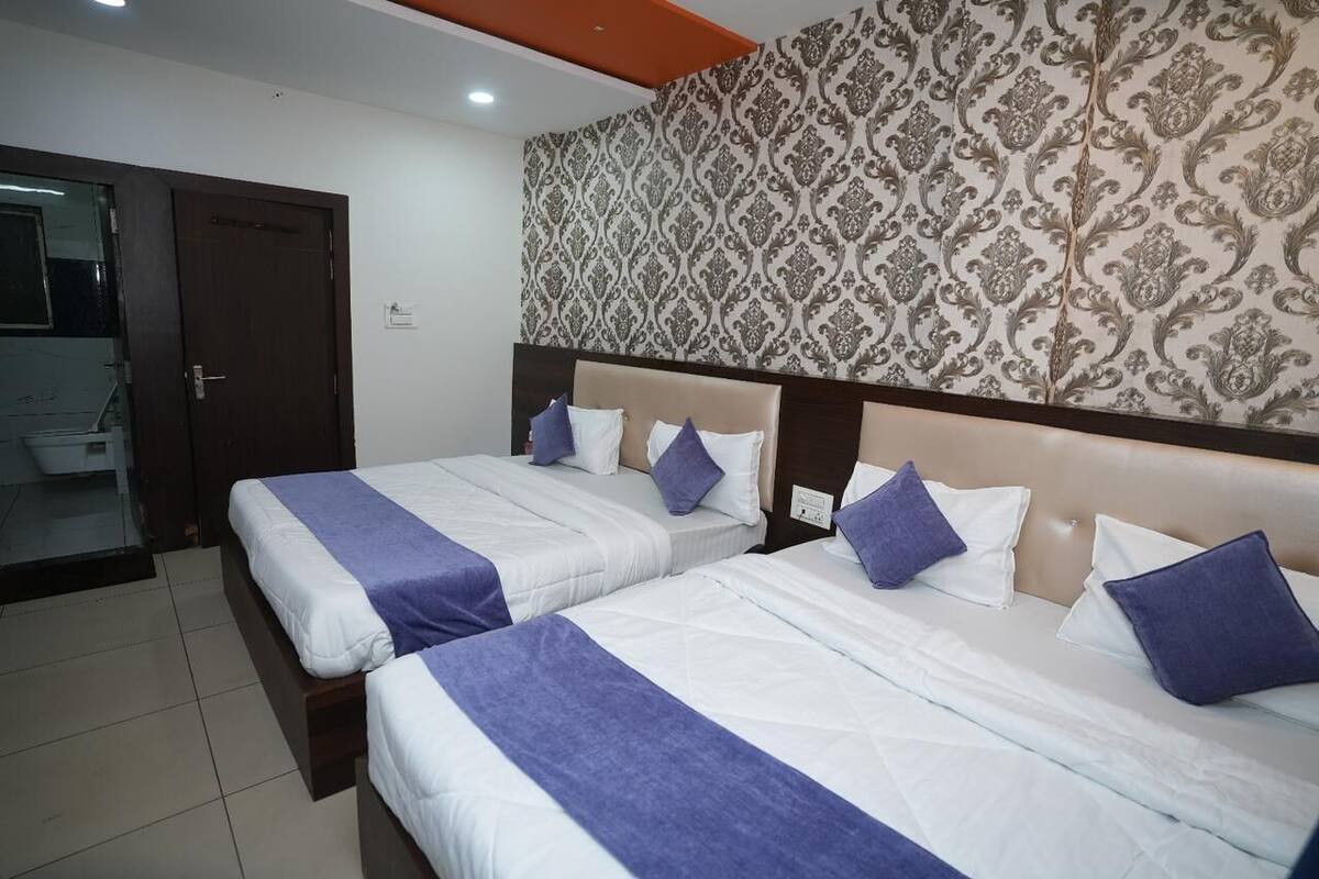 Habitación de hotel con dos camas, cada una con ropa blanca y detalles morados, un papel tapiz estampado y una puerta de madera.