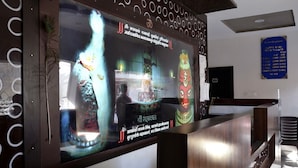 Een receptiezone met een groot digitaal scherm, een receptiebalie en een blauw bord met informatie over het hotel.