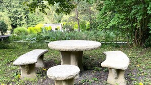 Ein Steintisch und Bänke in einem Garten mit Teich und Bäumen.