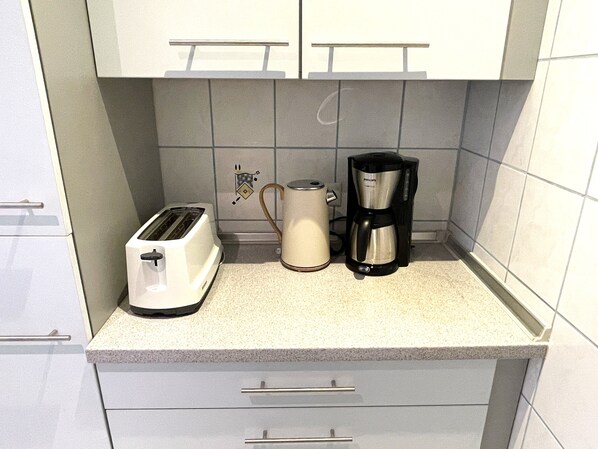 Una cocina con armarios blancos, un tostador, una cafetera y un hervidor sobre la encimera.