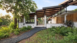 A modern house with a covered patio, a gravel pathway, and lush greenery.