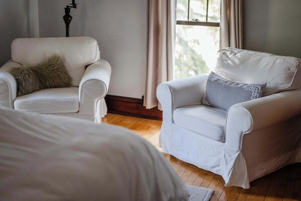 A room with two white upholstered chairs, one with a fur pillow and the other with a geometric pillow.