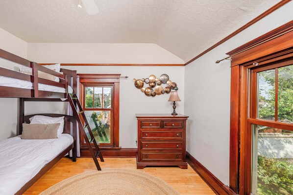 A room with a bunk bed, a wooden dresser, a lamp, and a window with a view of greenery. - Charming Family Home Steps from UWSP & Downtown (Stevens Point)