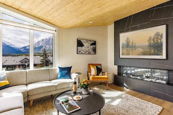 A living room with a sofa, a coffee table, a fireplace, and a large window with a mountain view.