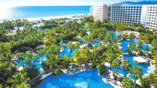 Un resort con varias piscinas rodeado de palmeras y vistas al océano.