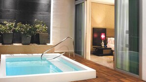 Una piscina rectangular interior con una escalera de metal, rodeada de plantas en macetas y una terraza de madera.