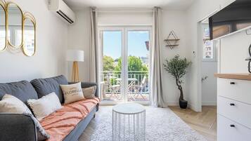 A modern living room with a grey sofa, a round white table, and a balcony with a view.