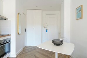 Een moderne keuken met een fornuis, oven en witte kasten. Er is een witte tafel met een zwarte mand in de eethoek.