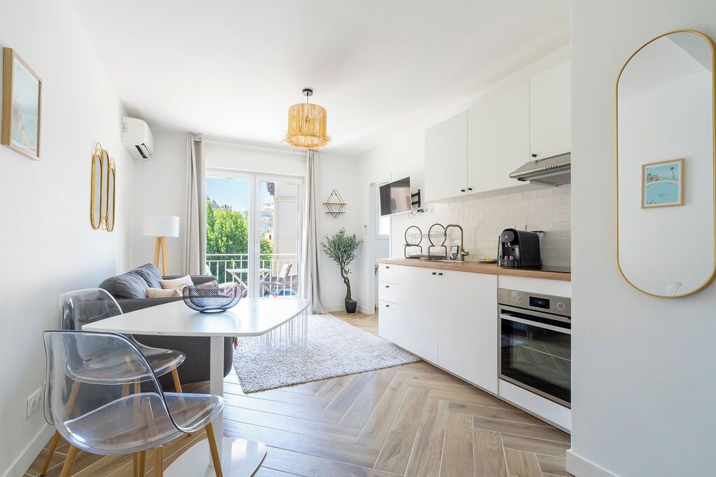 A modern kitchen with white cabinets, a dining area with a table and chairs, and a view of greenery outside.