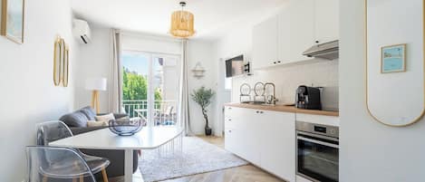 A modern kitchen with white cabinets, a dining area with a table and chairs, and a view of greenery outside.