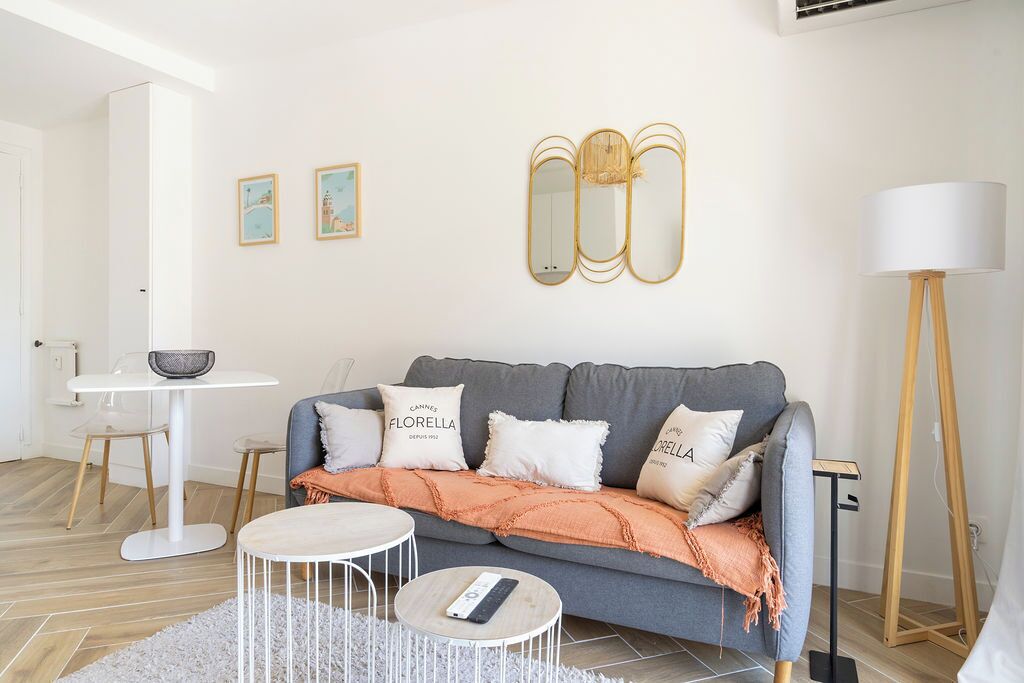 Ein Wohnzimmer mit grauem Sofa, weißen Kissen, einem runden Couchtisch, einem kleinen Beistelltisch und einer Stehlampe.