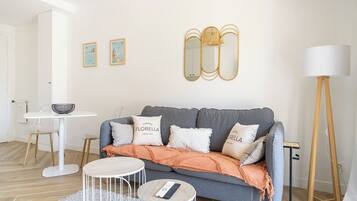 Ein Wohnzimmer mit grauem Sofa, weißen Kissen, einem runden Couchtisch, einem kleinen Beistelltisch und einer Stehlampe.