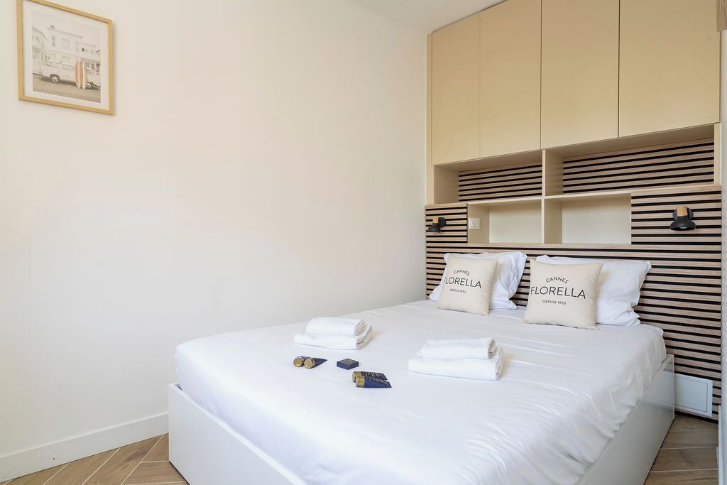 A neatly made bed with pillows, a framed picture on the wall, and a built-in wardrobe with horizontal slats.