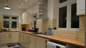 Eine moderne Küche mit beigen Schränken, einer Holz Arbeitsplatte, einem eingebauten Waschmaschine und einem Fenster mit Jalousien.