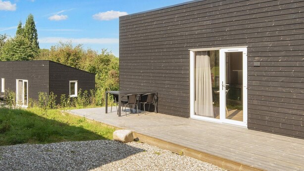 A modern building with a dark exterior, a wooden deck, and a glass door entrance. - Great Cabin in Camping Resort (Aabenraa)