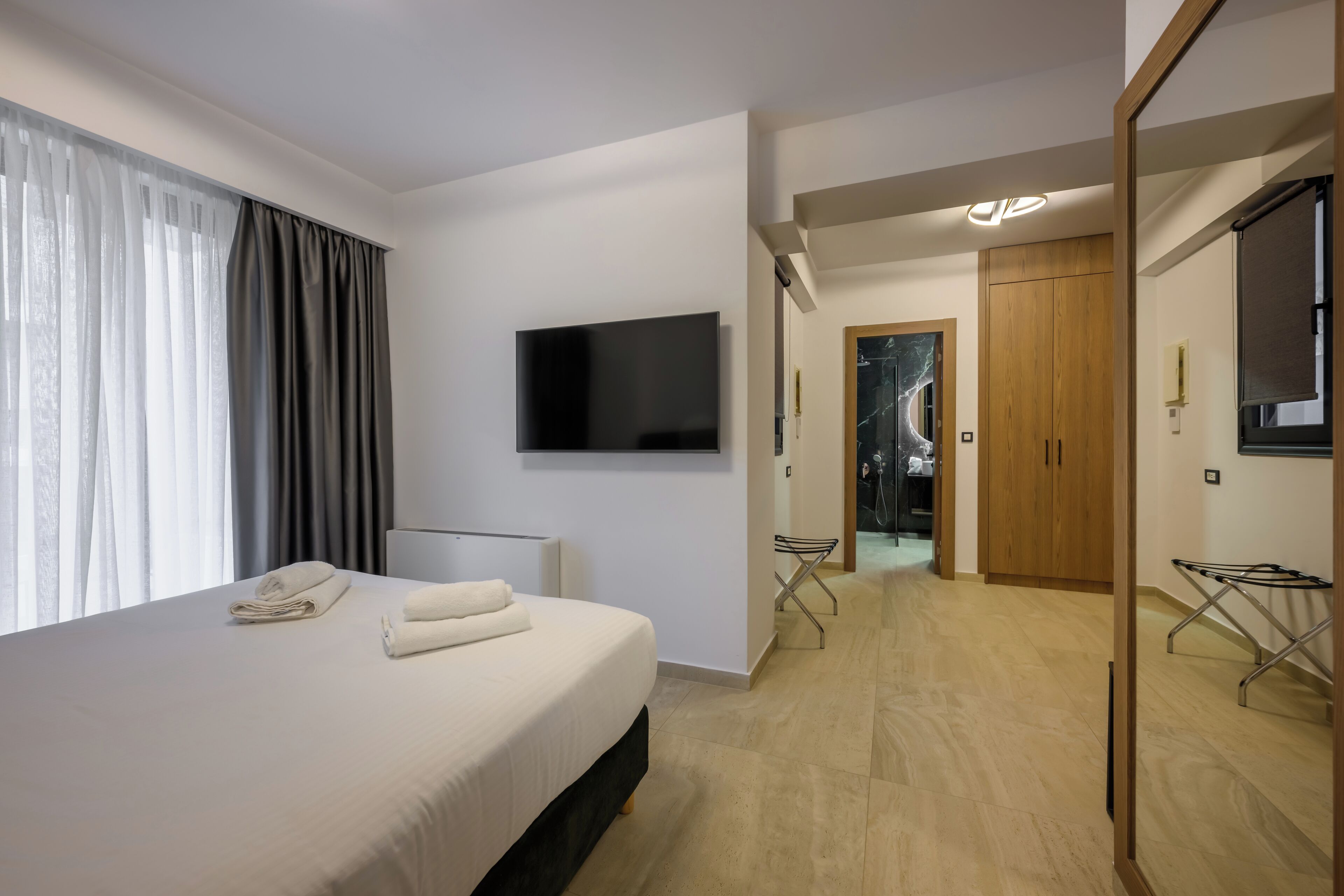 Een moderne hotelkamer met een groot bed, een flatscreen televisie aan de muur, een houten garderobe en een inloopkast.
