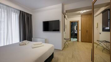 Een moderne hotelkamer met een groot bed, een flatscreen televisie aan de muur, een houten garderobe en een inloopkast.