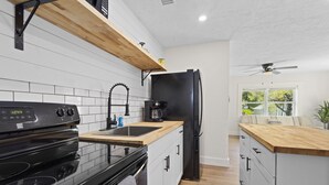 Una cocina moderna con armarios blancos, un refrigerador negro, una encimera de madera y un horno empotrado.