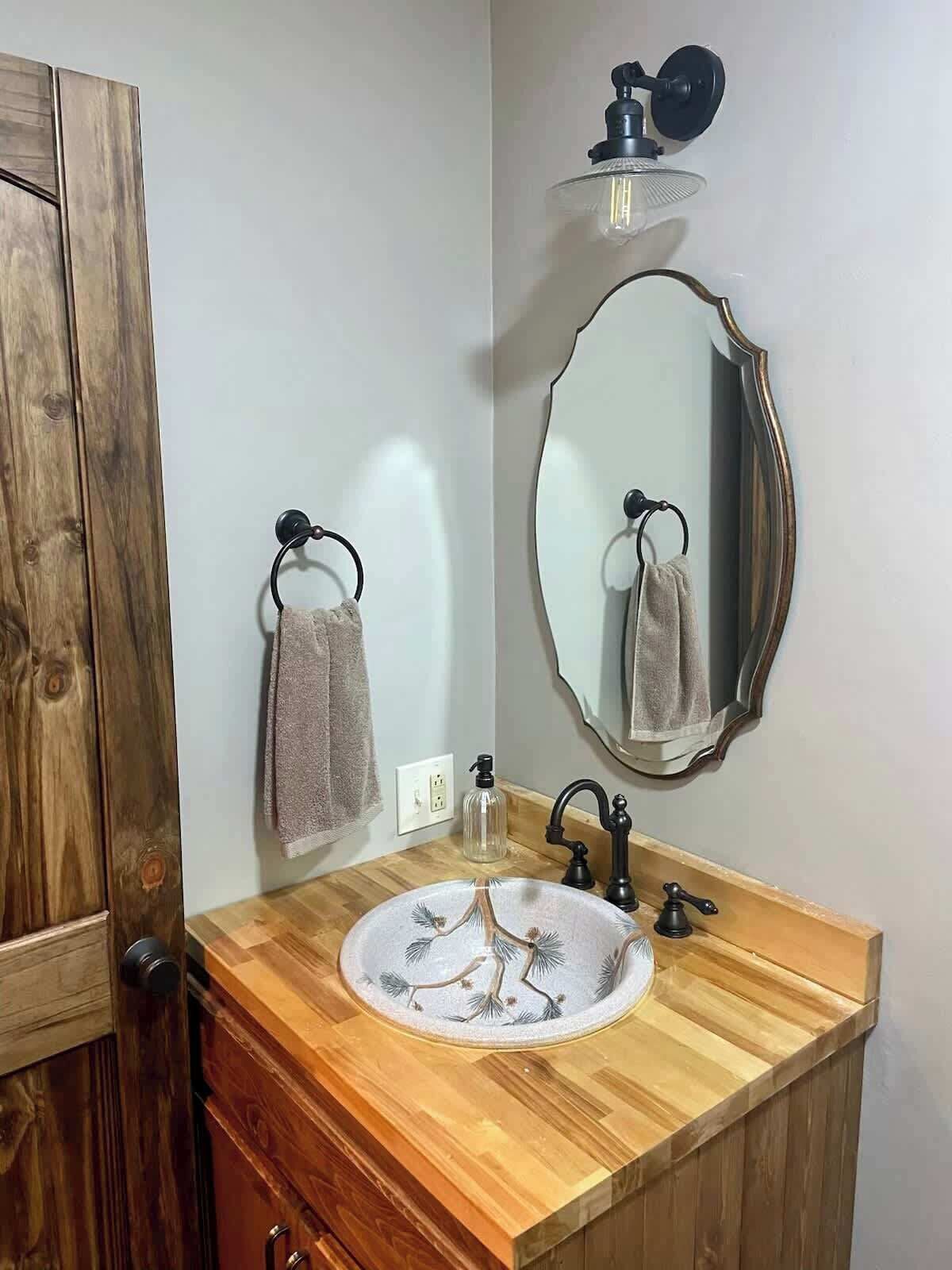 Un bagno con un mobile lavabo in legno, uno specchio rotondo, un portasciugamani e un lampadario a parete.