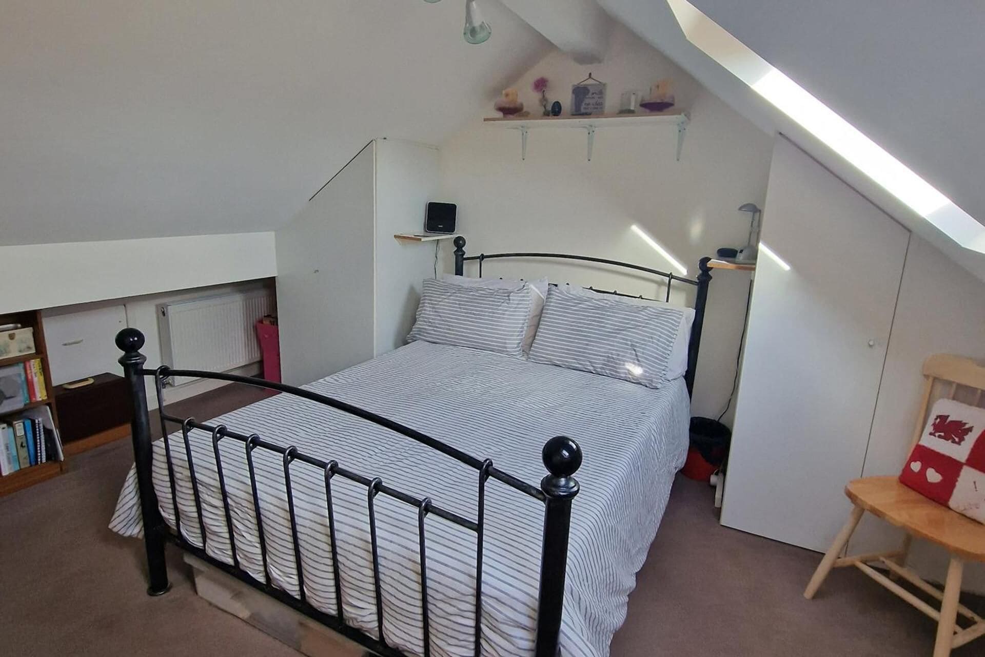 Une chambre à coucher comprenant un lit, un radiateur, une étagère avec des objets décoratifs et une chaise.