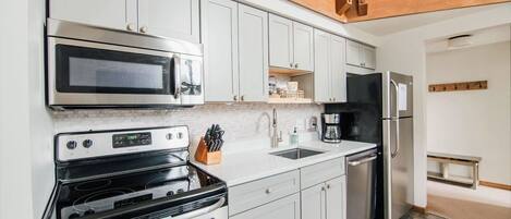 A modern kitchen with white cabinets, stainless steel appliances, and a wooden ceiling.
