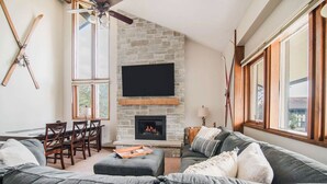 Ein Wohnzimmer mit Kamin aus Stein, einem darüber montierten Fernseher und einem großen Fenster.